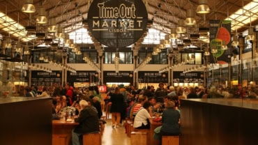 Modern shopping mall food court with seating area and visitors in black and white.