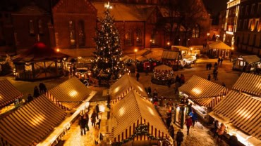 Vibrant street in Riga at night with festive holiday lights, outdoor cafes, and shoppers, capturing lively urban atmosphere.