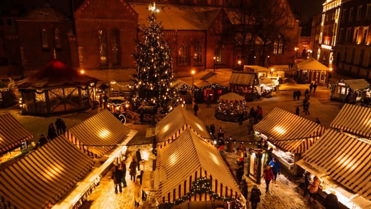 Vibrant street in Riga at night with festive holiday lights, outdoor cafes, and shoppers, capturing lively urban atmosphere.