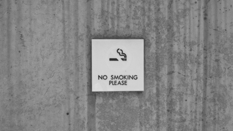 No smoking sign on brick wall promoting workplace health and customer satisfaction.
