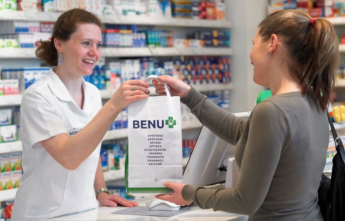 BENU pharmacist handing a bag with medicine to the customer.
