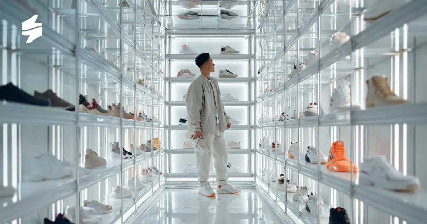 A customer shopping in a sneaker store with illuminated shelves showcasing a variety of athletic shoes.